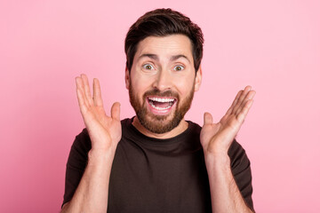 Photo of overjoyed funky guy with stubble brunet hair dressed brown t-shirt raising palms up staring isolated on pink color background