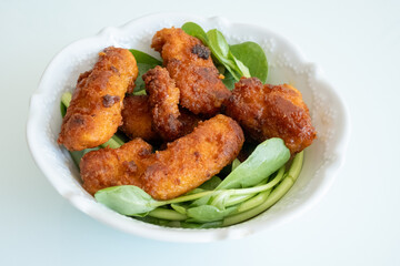 Fried chicken breast in bite-sized pieces with greens in a white bowl close-up