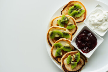 Plate of pancakes dripping with cherry jam, sour cream and kiwi pieces with white background.. Copy space for text. Mockup for menu, Pancake day