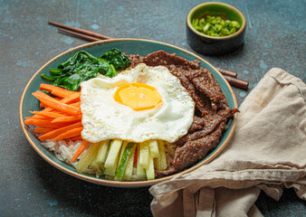 Plate of bibimbap, a mixed rice dish with meat and assorted vegetables, traditional Korean cuisine. The dish is seasoned with gochujang - chili pepper paste - and topped with a fried egg