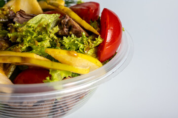 summer salad, tomato salad, vegetables, in a plastic container on a light background, food delivery, takeaway food