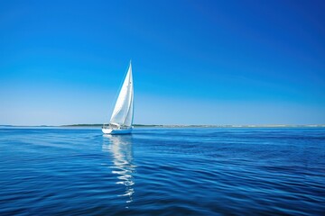 Fototapeta premium A sailboat gliding across calm blue waters under a clear summer sky