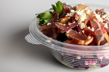 spring summer salad of beets and meat greens in a portable container on a light background, fast food delivery