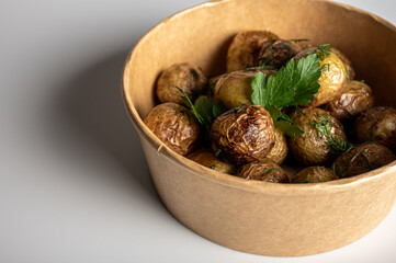 fried new potatoes cooked with golden skin, fast food delivery in kraft paper packaging on light background, place for inscription