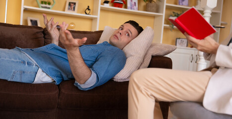 Sad exhaust young man patient lying on the couch on session with female psychologist in her office. Psychological help in desperate. Psychotherapy treatment of depression. Mental stability, health