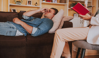 Sad exhaust young man patient lying on the couch on session with female psychologist in her office....