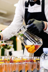 Bartender Pouring Fresh Fruit Cocktail in Glasses. Bartender in black gloves and apron pouring fresh fruit cocktail into glasses at a formal event. Vertical shot.