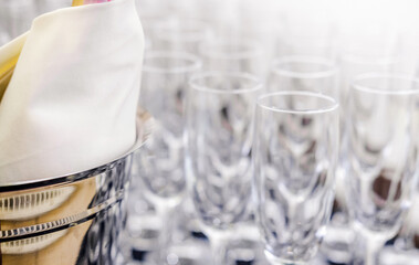 Empty Glasses and Wrapped Bottle at Event. Empty glasses arranged in rows with a bottle wrapped in a white cloth in the foreground. Horizontal shot.