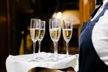 Waiter Serving Champagne Flutes on a Tray. Waiter in uniform serving champagne flutes on a tray with a white cloth. Horizontal shot.