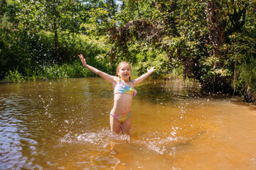 Fototapeta premium a girl child bathes in the water of the river laughter joy splashes summer heat