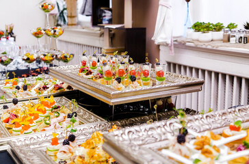 Buffet Table with Silver Trays. A buffet table at an event, covered with a black tablecloth, featuring a variety of appetizers displayed on elegant silver trays.