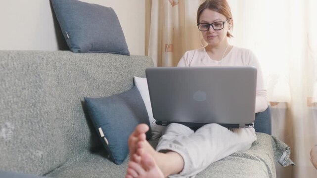 Young woman freelancer working home on laptop sitting on the couch bare feet.