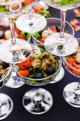 Pyramid of Fresh Salad Glasses. Pyramid of glasses filled with vibrant salads, featuring tomatoes, olives, and greens on a dark surface. Vertical photo. Top view.