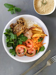 selective focus on lunchbox with tomato, watercress and carrot salad, with pork, potatoes and rice accompanied by farofa on a blurred gray background with space for text