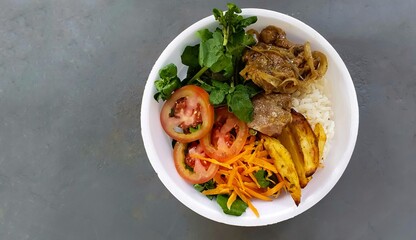  lunchbox with tomato, watercress and carrot salad, with pork, potatoes and rice on a blurred gray background with space for text