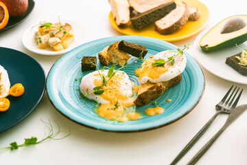 Poached eggs on a toasted slice, bread or toast on a turquoise plate, next to avocado, cheese, tomatoes and cutlery. Delicious and healthy breakfast. View from above.