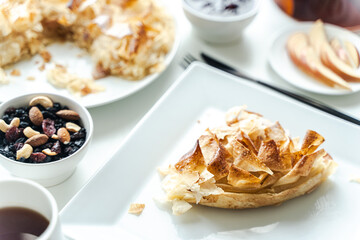 Apple dessert, fila pastry pie on a square white plate with a cup of tea and nuts on a light background.