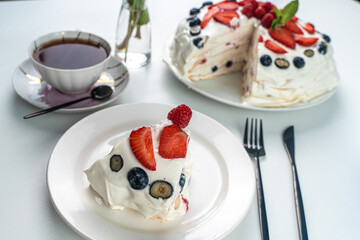 Pavlova cake or meringue dessert with berries on a white table and a cup of black tea. Close-up, focus selected