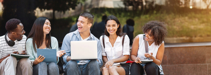 Joyful University Students Sitting At Campus With Laptop And Laughing Together, Having Break In Lessons, Panorama