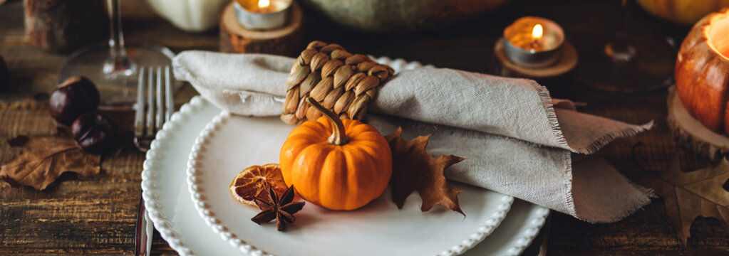Atmospheric autumn elegant beautiful table setting with pumpkins for a wedding or thanksgiving family celebration. Fall decoration countryside rustic style, cozy home atmosphere , candles, wine banner