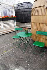 Two dark green metal chairs next to the table. Wooden igloo (sauna) textured surface of background. Weather after the rain. Noblessner, Tallinn, Estonia, Europe. July 2024.