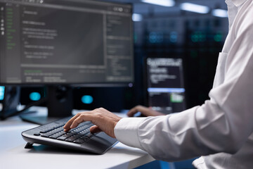 IT administrator working on PC in hardware room housing server rackmounts, storage devices and...