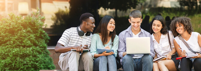 Group Of University Students Using Laptop Outdoors, Preparing For Classes Together, Sitting On Bench In Park