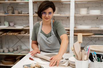 Rolling wooden stick to make flat sheet of clay. Preparing clay for cutting and assembling it. Slab building method in ceramics crafting.