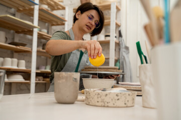 Washing off the sponge before applying moisture on a clay product. Cleaning a sponge tool before smoothing the surface of a pottery project.