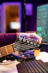 Skilled musician tuning his acoustic guitar strings to record new audio files in a home studio...