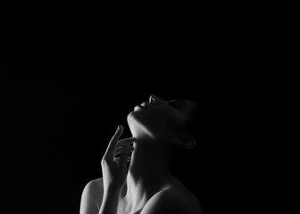 A black and white portrait of a woman with her head tilted upwards, touching her neck with her hand. The background is dark, creating a dramatic contrast, copy space above