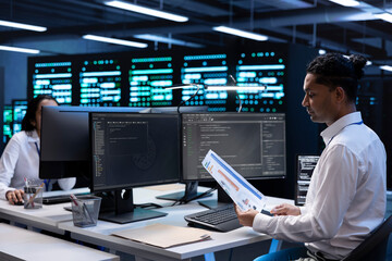 Engineer in data center doing yearly maintenance checkup to prolong hardware life span, looking over documents, monitoring server infrastructure and reading specifications paperwork