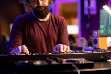 Audio engineer pressing keys of electric synthesizer and composing new song, adjusting volume...