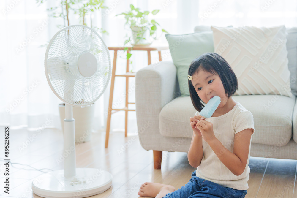 Wall mural 夏休みに扇風機の前でアイスを食べる子供