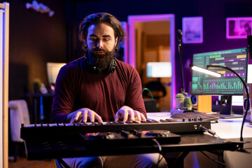 Skilled producer creating new music on piano midi controller, working with mixing console and daw...