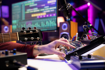 Sound engineer using mixing console and acoustic guitar in home studio, adjusting volume levels in...