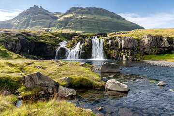 Waterfall cascading over rocks with lush green mountain under clear blue sky
