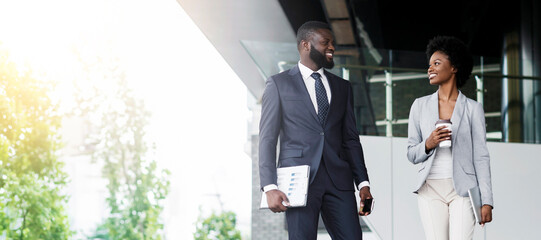 Handsome african businessman and attractive black businesswoman discussing work while walking...