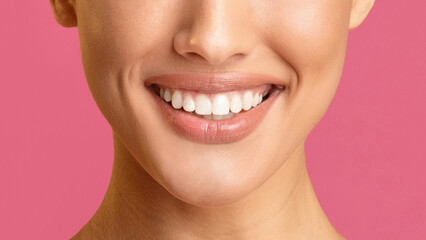 Obraz premium This image shows a close-up view of a womans mouth smiling with her teeth showing. The background is a solid pink color. The focus is on the womans teeth, which are white and straight.