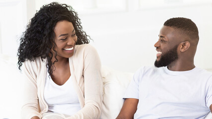Obraz premium A happy couple sits together on a couch in a light-filled room. They are both smiling and looking at each other.