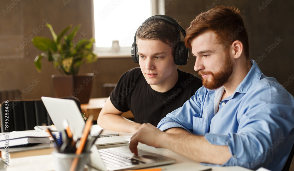 Aufkleber two guys are seated at a desk in an office environment, focused on a laptop screen. they appear to b