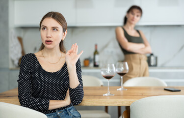 Offended middle-aged woman sitting in the kitchen while other woman talking angrily to her