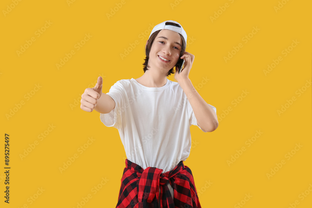 Poster Cool teenage boy talking by mobile phone on yellow background