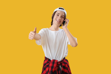 Cool teenage boy talking by mobile phone on yellow background