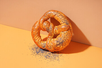 Delicious pretzel with poppy seeds on color background