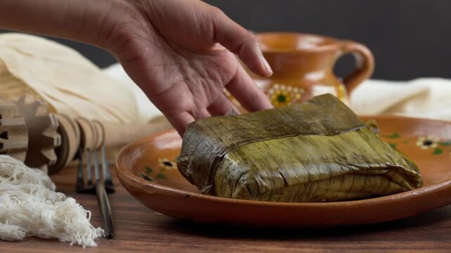Mexican woman places a Jarocho tamal wrapped with banana leaf on a clay plate, Food of Mexico Tamal Veracruz style