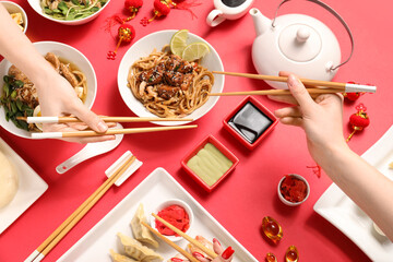 Female hands with chopsticks and different Chinese dishes on red background