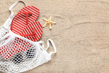 String bag with flip-flops, sunglasses and starfish on sand