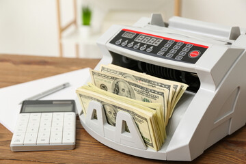 Modern cash counting machine with dollar banknotes and calculator on table in office