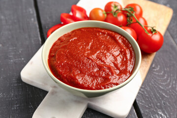 Bowl with tasty tomato paste on dark wooden background, closeup